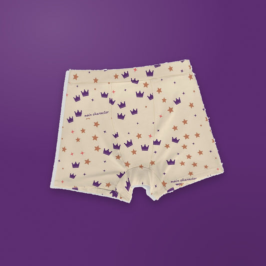 Main Character men's boxer briefs laid flat on a plum background: cream fabric printed with purple crowns, terracotta and coral stars and tiny sparkles