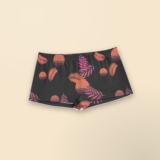 Out of Office women's boxer briefs laid flat on a butter-yellow background: charcoal fabric printed with coral and magenta palm leaves and striped sunset circles
