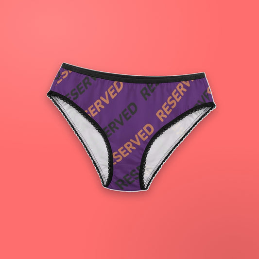 Reserved women's lace briefs laid flat on a coral background: purple fabric with the word RESERVED repeated diagonally in terracotta and charcoal, black waistband and lace leg trim